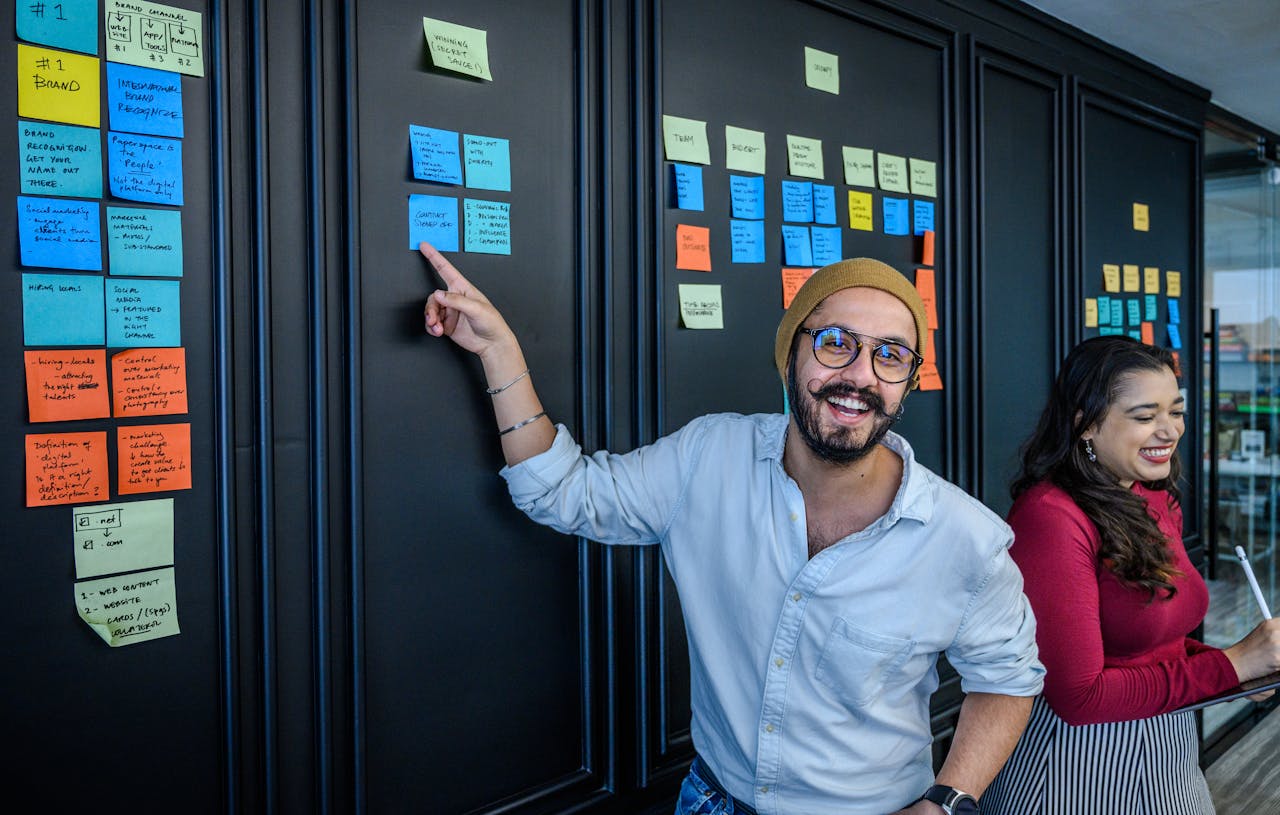 Cheerful entrepreneurs brainstorming ideas on sticky notes during a meeting indoors.